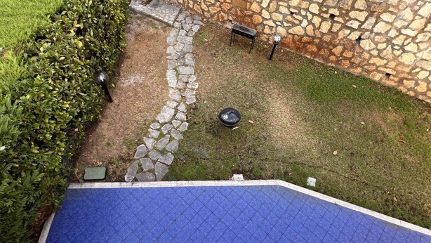 A rooftop pool area with a stone wall, a small grill, and a seating area.
