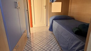 A compact room with a single bed, a door, and a small window.