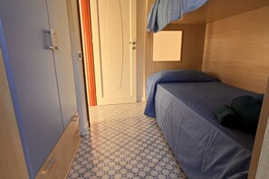 A compact room with a single bed, a door, and a small window.