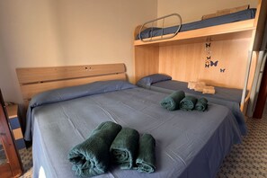 A room with two beds, one with a bunk bed above it, and a wooden headboard.