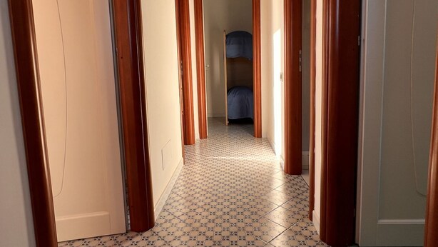 Un pasillo con baldosas de diseño, puertas de madera y vista a una habitación con cama.