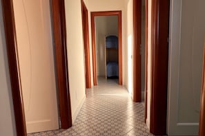 A hallway with patterned floor tiles, wooden doors, and a view into a room with a bed. - Villa with garden just minutes from the sea (Sparvasile)