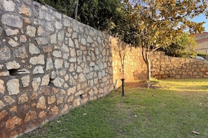 A stone wall with a small opening, a grassy area, and a tree. - Villa with garden just minutes from the sea (Sparvasile)