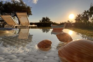 A glass-top pool with lounge chairs and seashells.