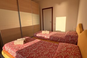 A hotel room with two beds, a wardrobe, a door, and a window.