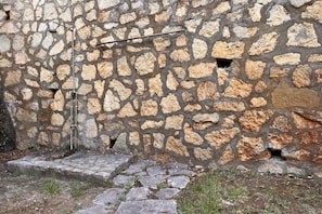 A stone wall with a metal structure, possibly a water feature, and a stone pathway leading to a door.