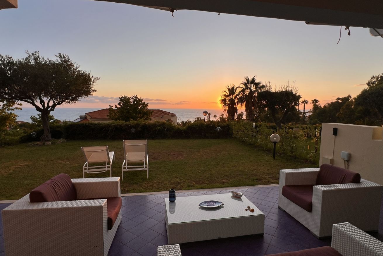 A patio with outdoor furniture, a dining table, and a view of the sunset over the sea.