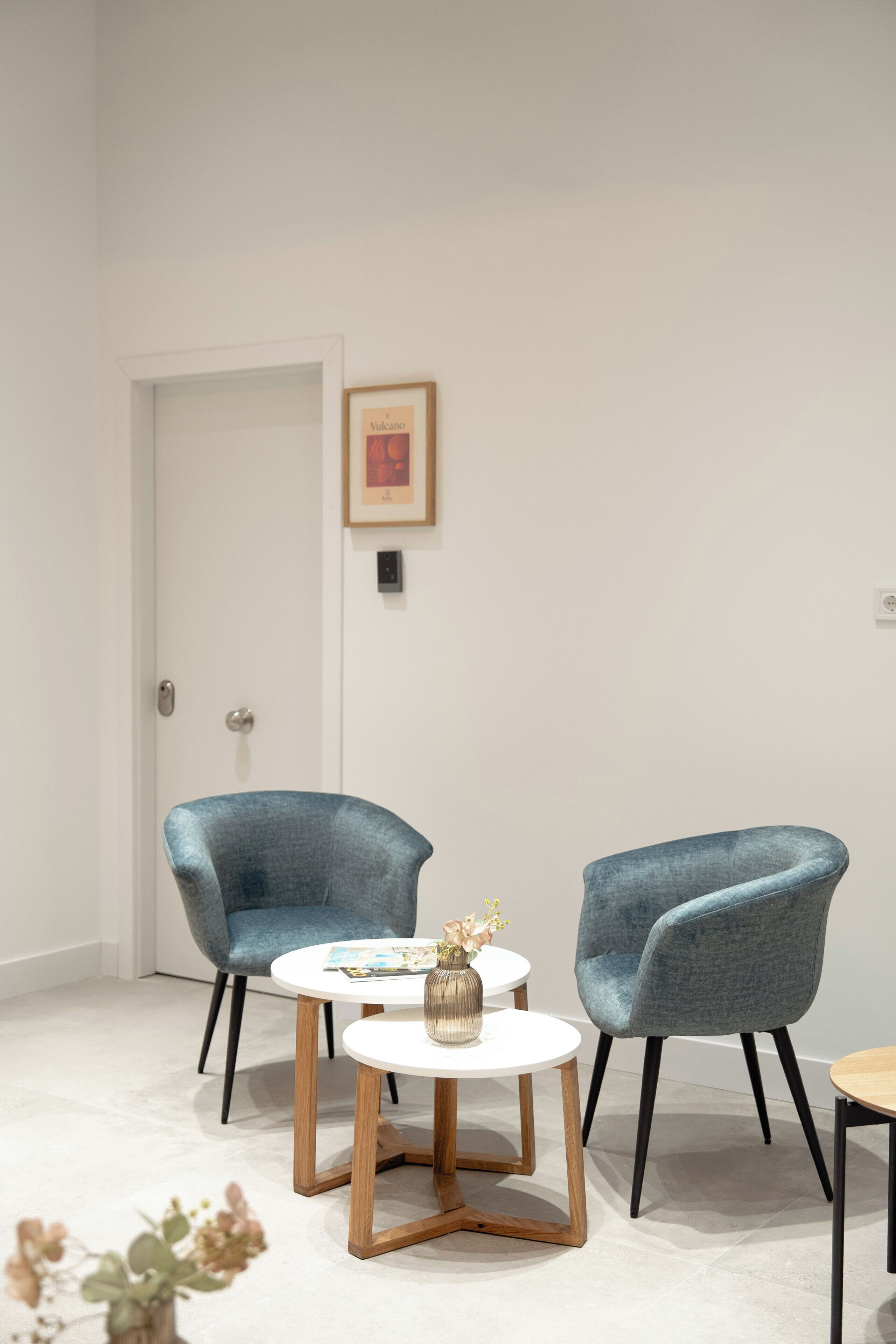 Ein Zimmer mit zwei blauen Sesseln, einem weißen runden Tisch und einem kleinen Tisch mit einer Vase.