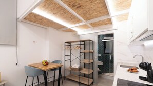 Una cocina compacta con una mesa de madera, taburetes de bar, un mueble de estanterías integrado y una cafetera moderna.