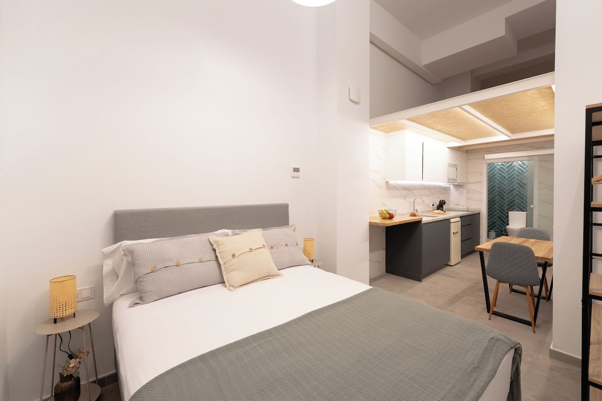 Ein modernes Schlafzimmer mit Bett, Nachttischen, einem Schreibtisch und einer Küchenzeile.