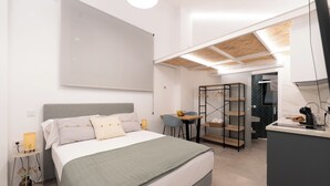 Un dormitorio moderno con cama, mesita de noche y un pequeño escritorio con silla y estanterías.