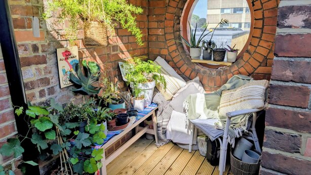 Un coin accueillant avec un mur en briques, une fenêtre ronde et diverses plantes en pot.