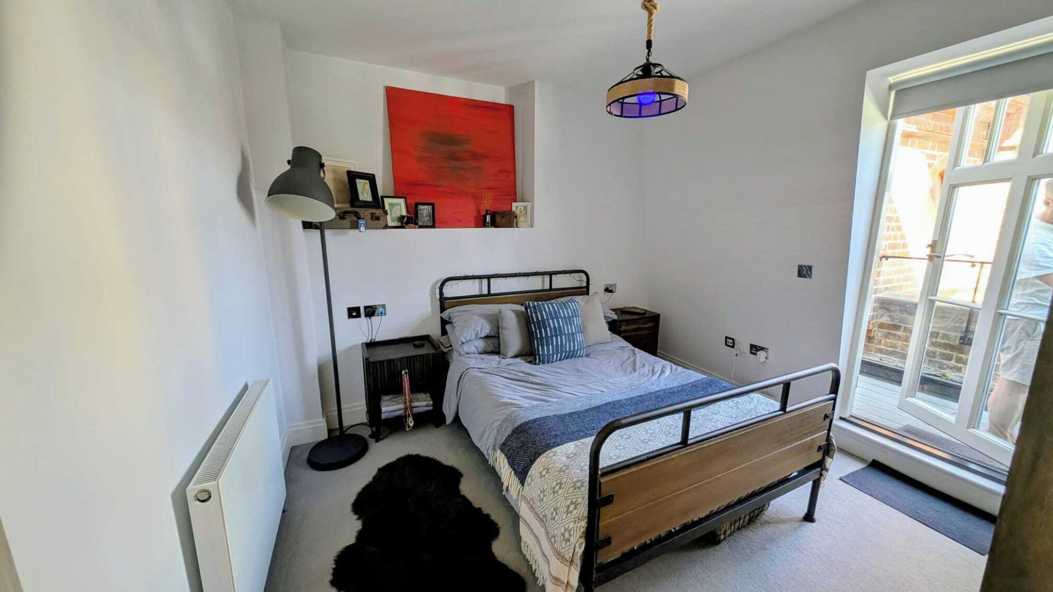 A bedroom with a bed, bedside table, lamp, and a red abstract painting on the wall.