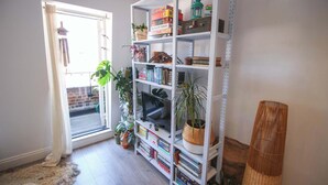 Une pièce avec une bibliothèque, un téléviseur et un lampadaire à pied en osier.