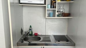 A compact kitchenette with a microwave, sink, and a small refrigerator. - Tiny Studio (München)