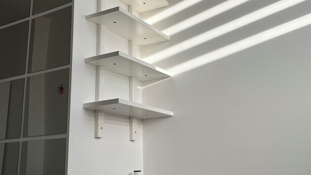 A bedroom with a bed, white shelves, and a window with blinds. - Tiny Studio (München)