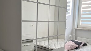 A bedroom with a mirrored wardrobe, a bed with pillows, and a window with blinds. - Tiny Studio (München)