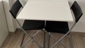 A small, white table with four black chairs in a corner. - Tiny Studio (München)