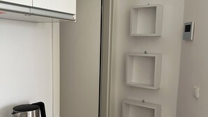A kitchen with white cabinets, a stainless steel kettle, and a remote control on the counter. - Tiny Studio (München)