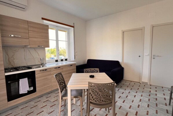 Una cocina compacta con una mesa y sillas, un sofá de color oscuro y un suelo estampado.
