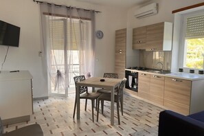 Une cuisine de taille réduite avec des meubles de rangement en bois, une table à manger avec des chaises et un téléviseur posé sur un meuble.