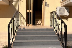 Un conjunto de escalones de hormigón que conducen a la entrada de un edificio, con barandillas metálicas a ambos lados.