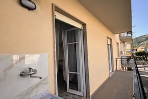 A balcony with a tiled floor, a door with a curtain, and a wall-mounted light fixture. - Cozy and modern apartment a stone's throw from the sea (Marina di Fuscaldo)