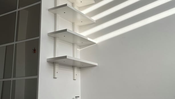 A bedroom with a bed, white shelves, and a window with blinds. - Tiny studio (München)