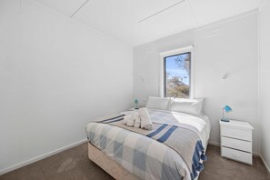 Ein Schlafzimmer mit einem Bett, einem Nachttisch, einem Fenster und Blick auf Bäume.