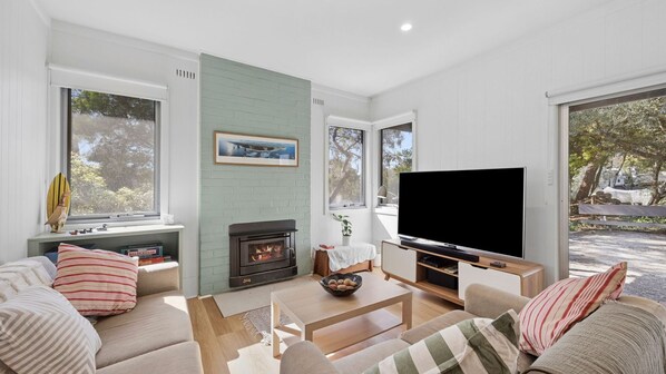 A modern living room with a fireplace, a flat-screen TV, and a comfortable seating area. - Cricklewood - A delightful holiday rental (Anglesea)