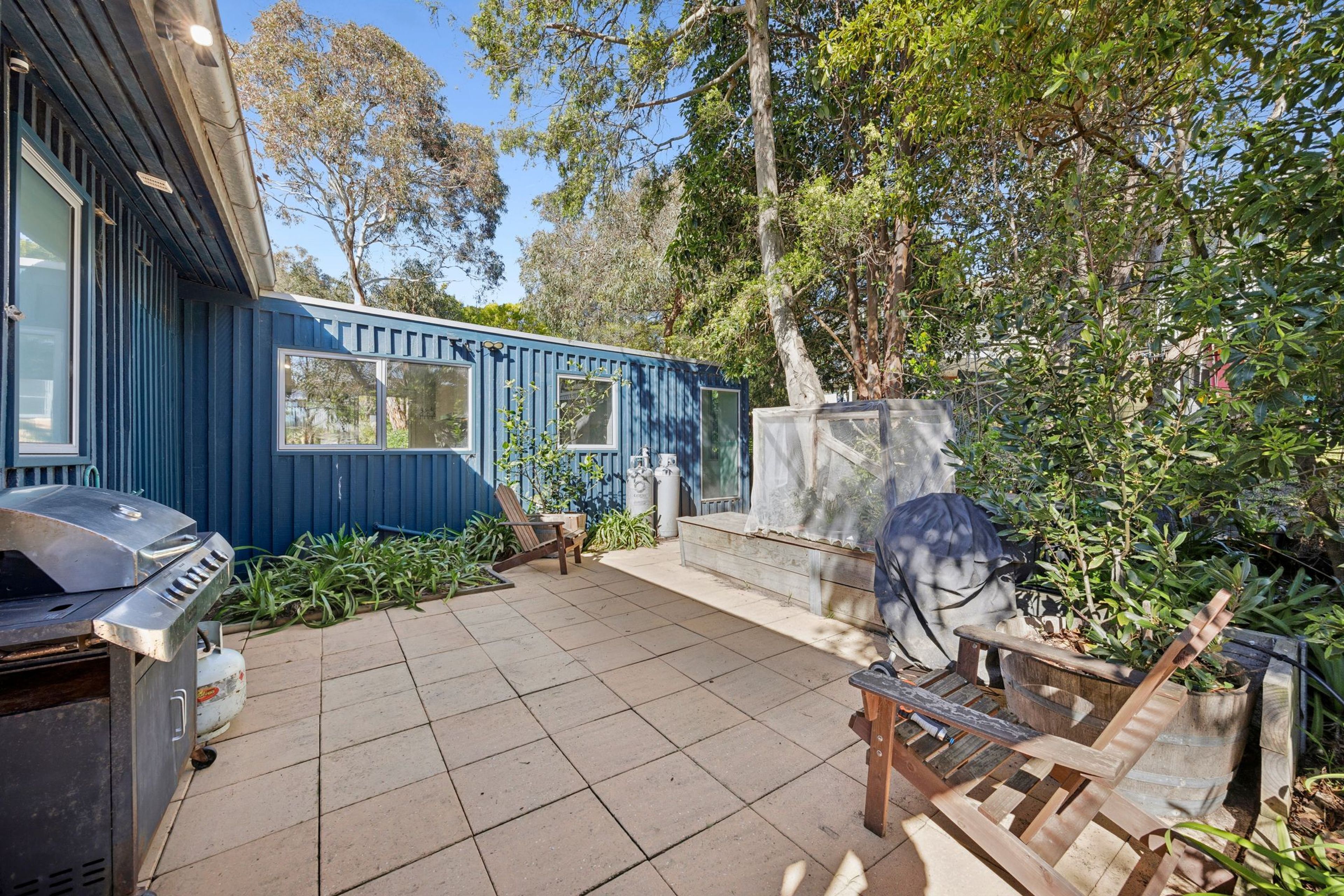 A blue house with a patio, a barbecue grill, and a wooden deck.