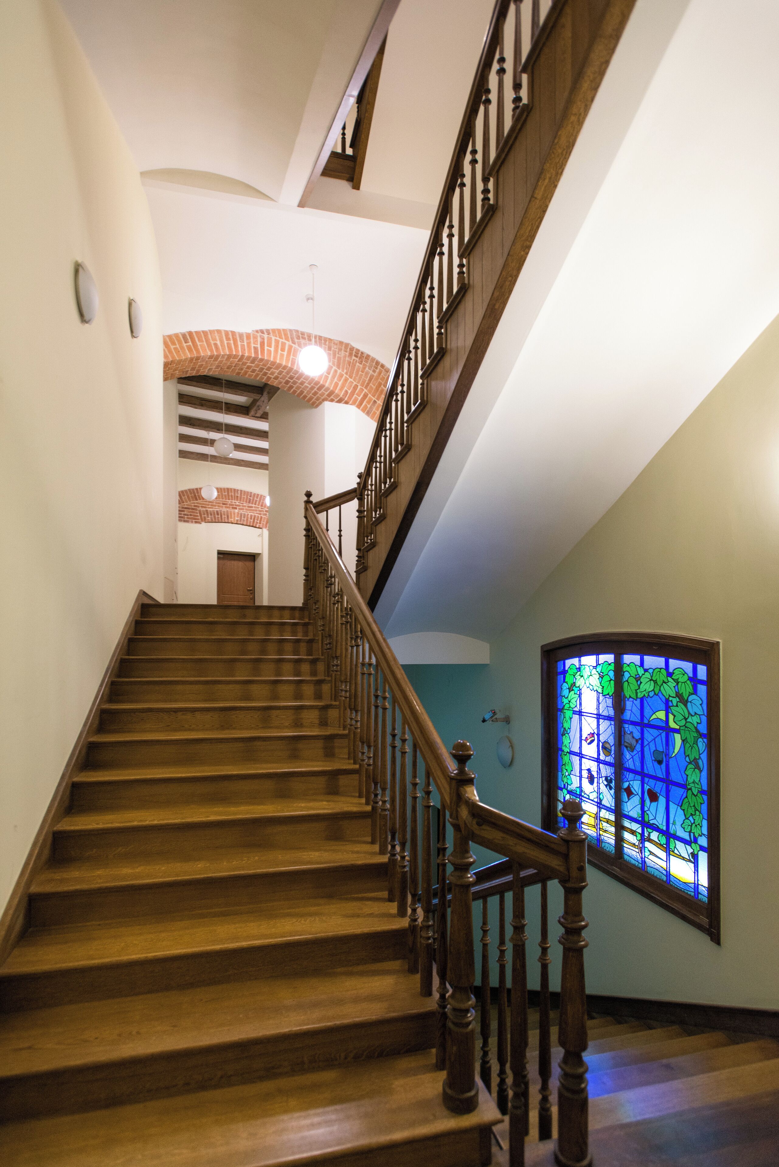 A wooden staircase with a handrail, leading to a landing with a door and a stained glass window.