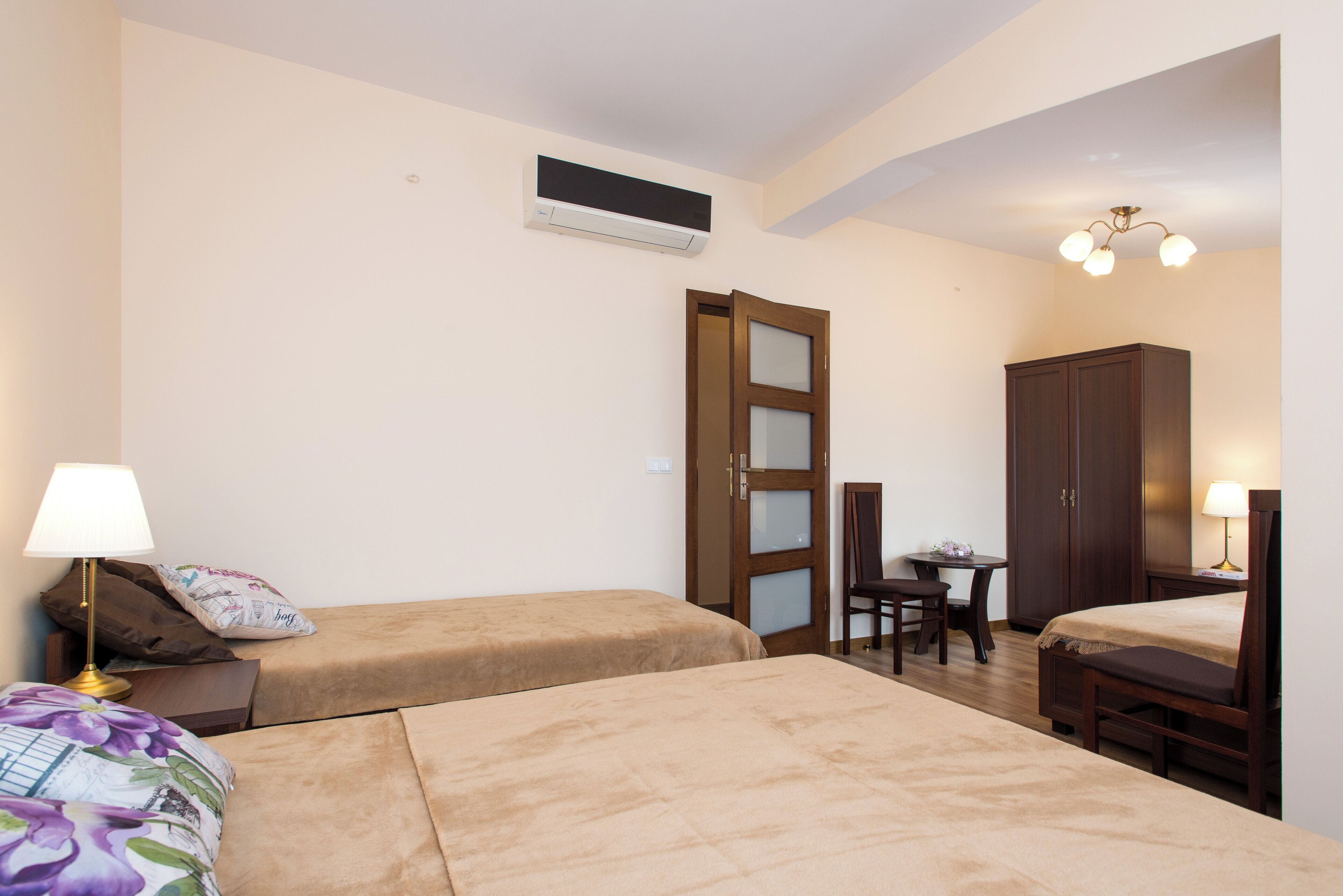 A hotel room with two beds, a desk, a chair, a wardrobe, and a lamp.