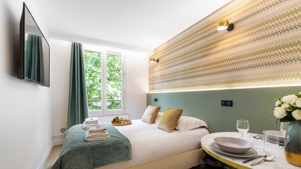 A hotel room with a bed, a dining table, and a view of greenery outside. - Spacious Studio - 2P - Beaugrenelle/eiffel Tower (Paris)