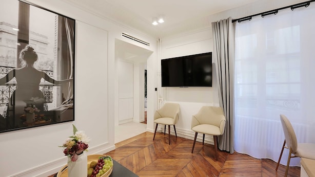 A modern living room with a large TV, two chairs, a wooden herringbone floor, and a large window with curtains. - Charming Apartment - 2br/6p - Gare Saint-lazare (Paris)