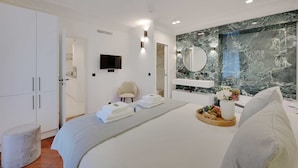 A modern hotel room with a large bed, a marble wall, a TV, and a tray of fruit. - Charming Apartment - 2br/6p - Gare Saint-lazare (Paris)