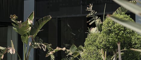 L’entrée d’un hôtel, avec une grande enseigne indiquant « NearYo Hotel ». On y trouve des plantes en pot et un petit espace aménagé en jardin devant l’entrée.