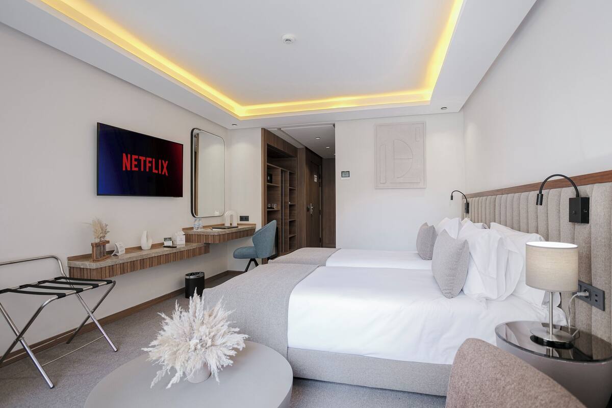 Une chambre d’hôtel moderne, dotée d’un grand lit, d’un bureau, d’une chaise et d’un téléviseur affichant le logo de Netflix.