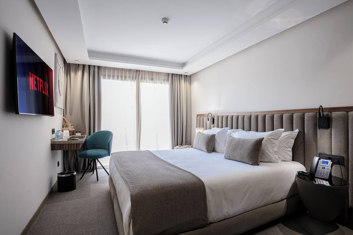 Une chambre d’hôtel avec un grand lit, un bureau avec une chaise, un téléviseur fixé au mur et un téléphone sur la table de chevet.