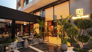 A hotel entrance with a modern design, featuring a glass facade, outdoor seating area with chairs and tables, and potted plants. - NearYo Hotels (Marrakech)
