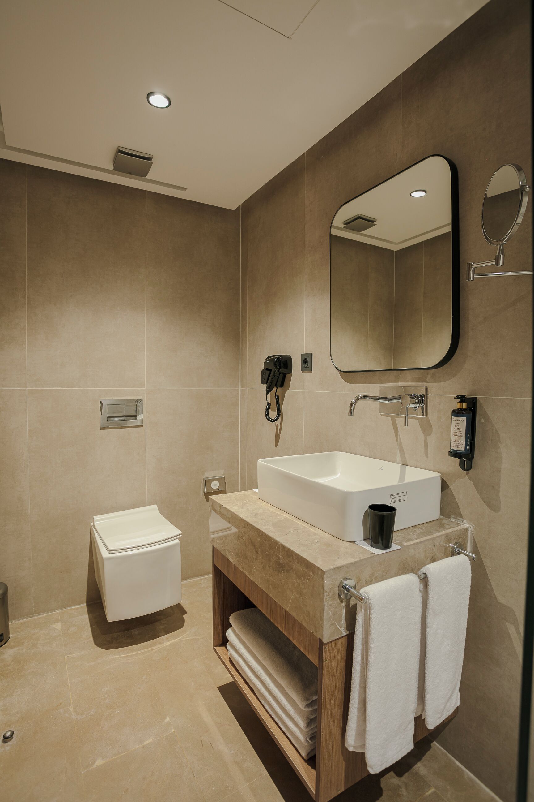 Un baño moderno con un lavamanos blanco, un espejo, un perchero para toallas y un inodoro.