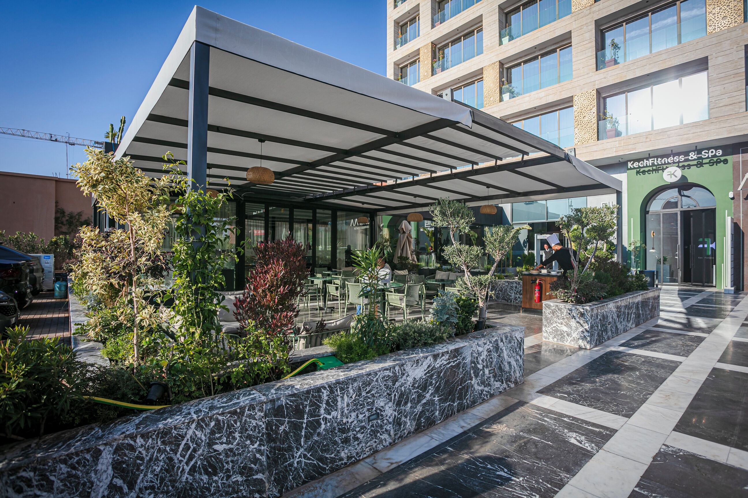 Una entrada de hotel moderna con un área de estar al aire libre techada, un mostrador de recepción y un letrero de spa.