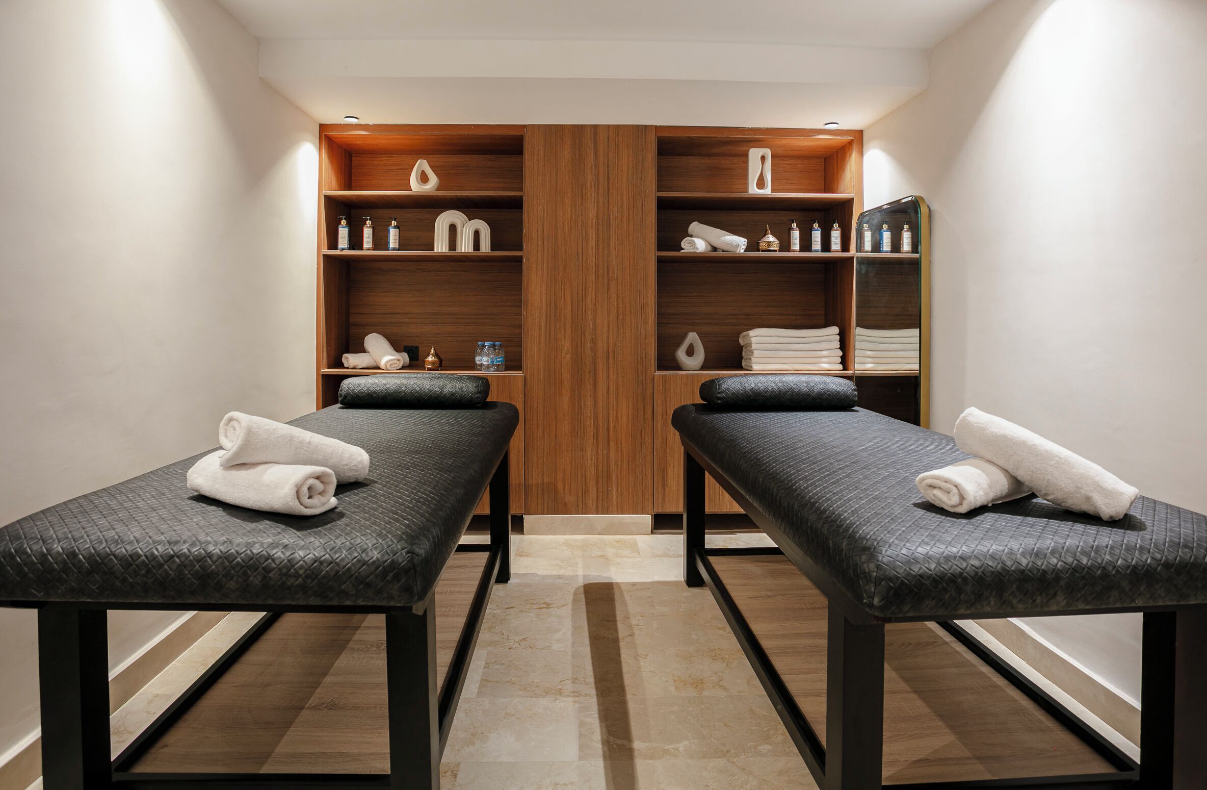Une salle de spa équipée de deux tables de massage, d’étagères en bois où sont rangées les serviettes et les articles de toilette, et d’une grande armoire en bois.