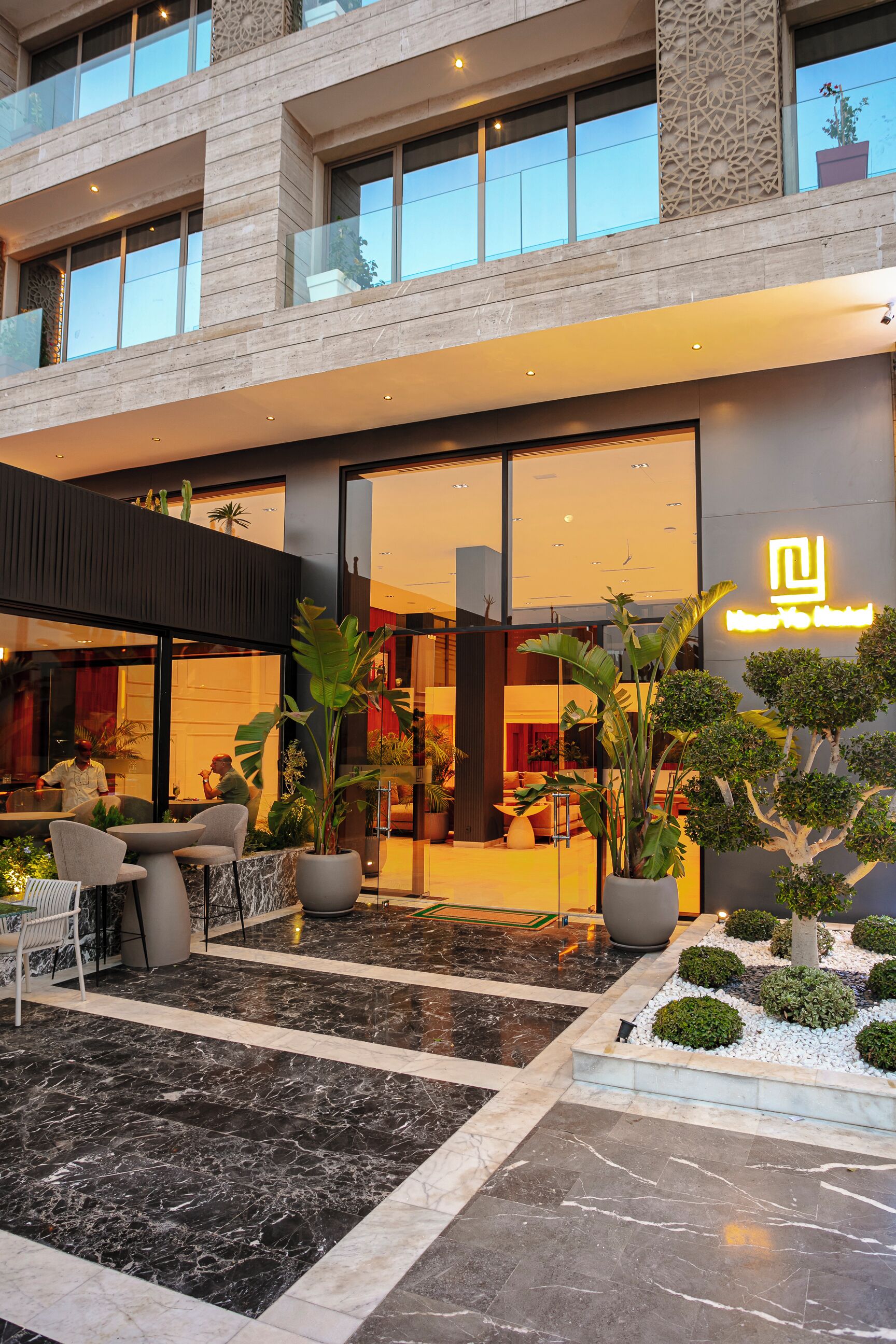 A modern hotel with a spacious outdoor area featuring marble flooring, potted plants, and outdoor seating.
