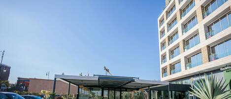 A modern hotel with a covered outdoor seating area, a parking lot, and a building with a sign that reads "INNEXUS."