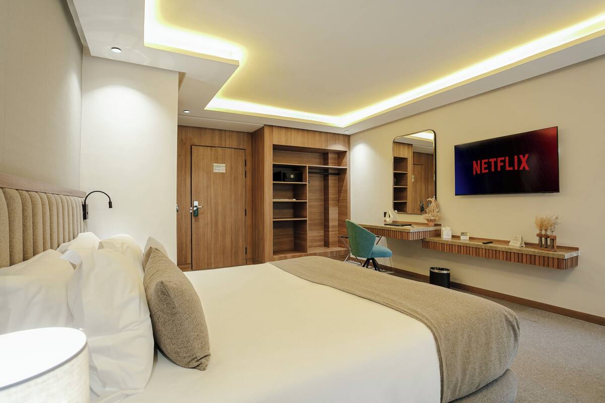 Une chambre d’hôtel moderne, dotée d’un grand lit, d’un bureau, d’une chaise, d’une armoire et d’un téléviseur affichant le logo de Netflix.