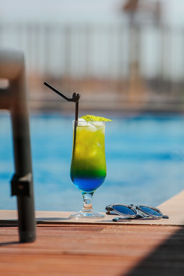 A cocktail glass with a straw and a lime garnish on a wooden table near a pool.