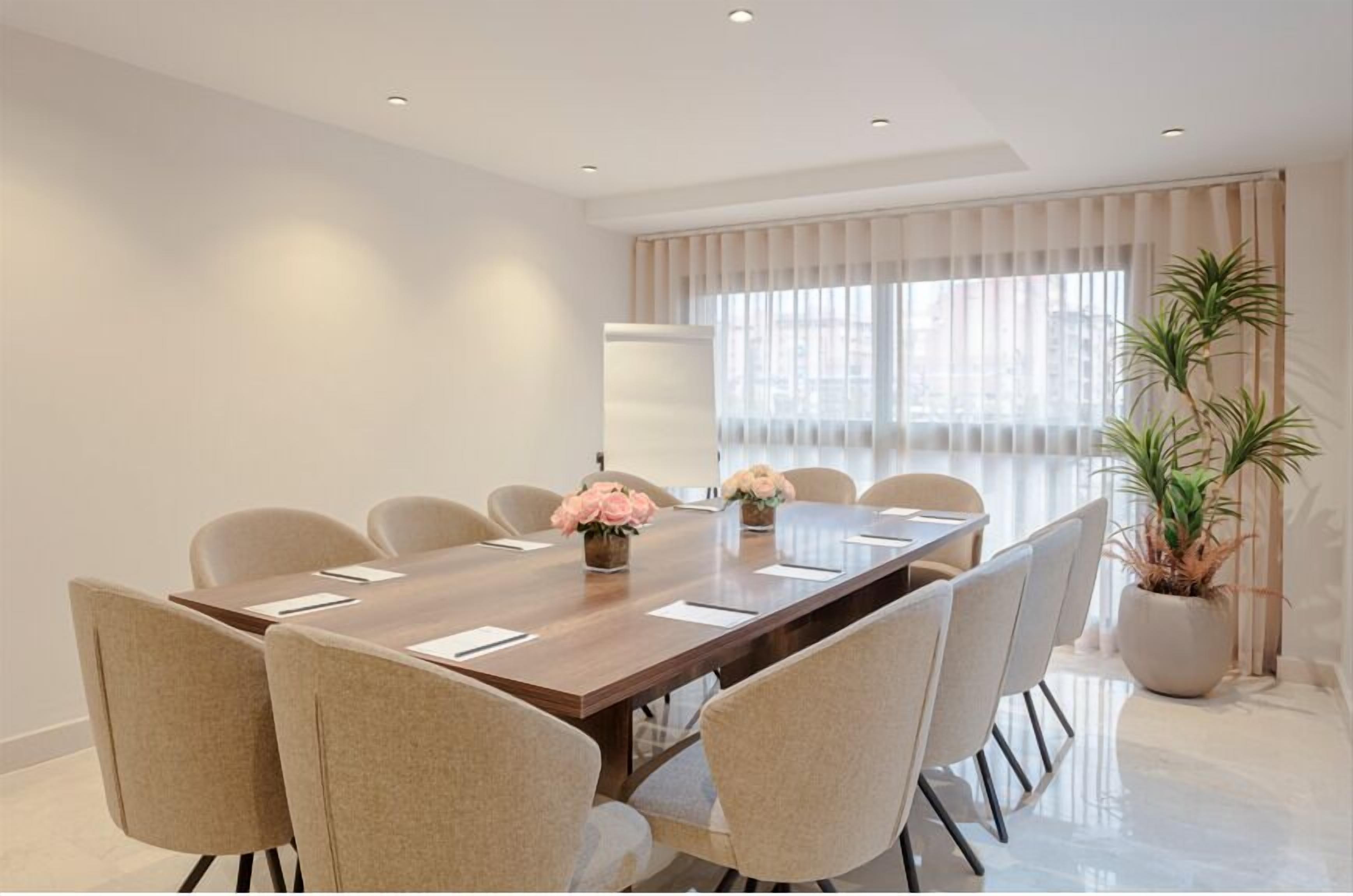 A modern conference room with a long table, beige chairs, and potted plants.
