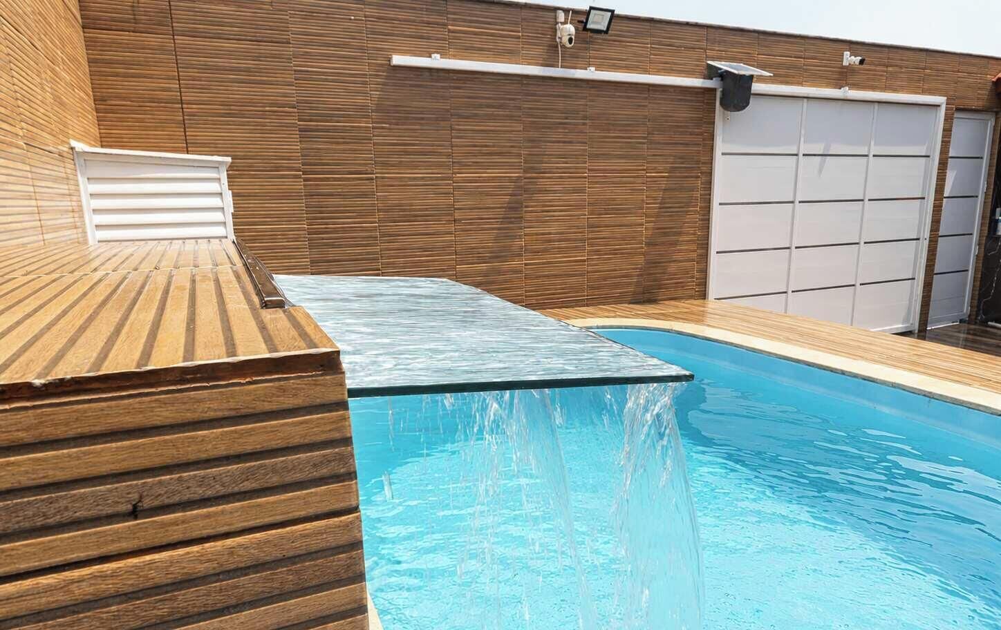 Una piscina con muelle de madera y un portón de garaje al fondo.
