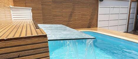 A swimming pool with a wooden deck and a garage door in the background.